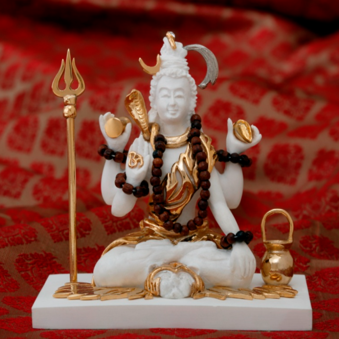 Statue of a deity with a trident, rosary, and other offerings on a red patterned fabric background